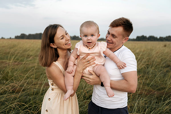 Cheerful mother and father carrying daughter together in field