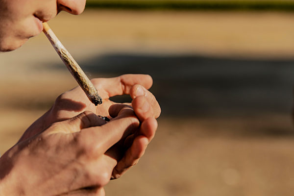 Teenage boy igniting marijuana joint during sunset
