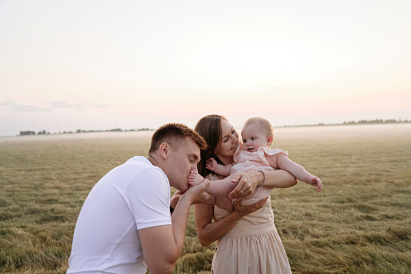Father kissing daughter's feet while mother carrying her on field