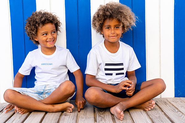Smiling brothers sitting on wooden walkway against striped wall