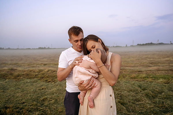 Mother and father embracing daughter together on field during sunset