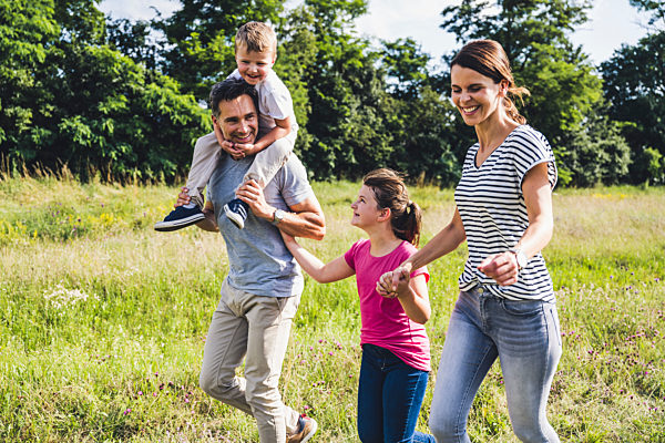 Father carrying son on shoulders while walking with family at meadow