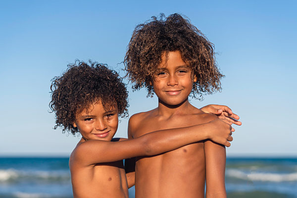 Brothers embracing at beach on sunny day