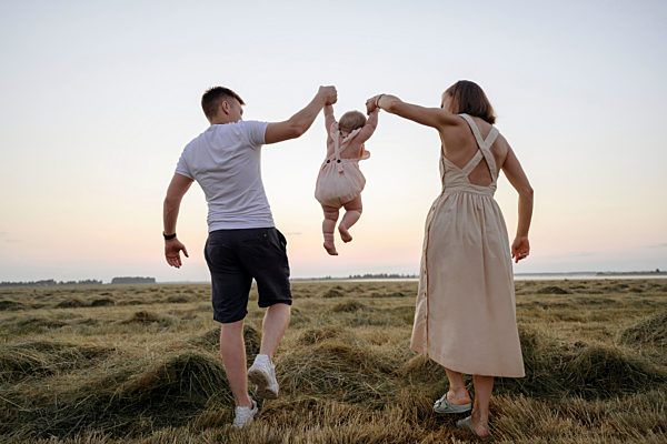 Parents swinging daughter while walking on field