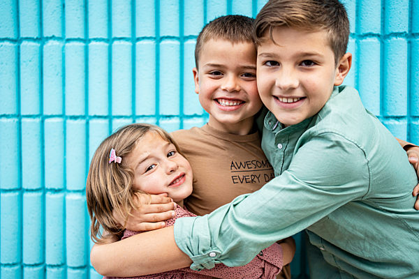 Siblings embracing each other in front of blue wall