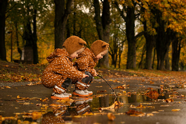 Twins crouching at puddle in autumn park