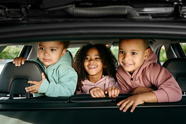 Smiling sisters with brother at back seat of car