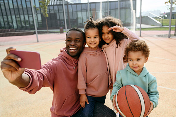 Father taking selfie with children through mobile phone at sports court