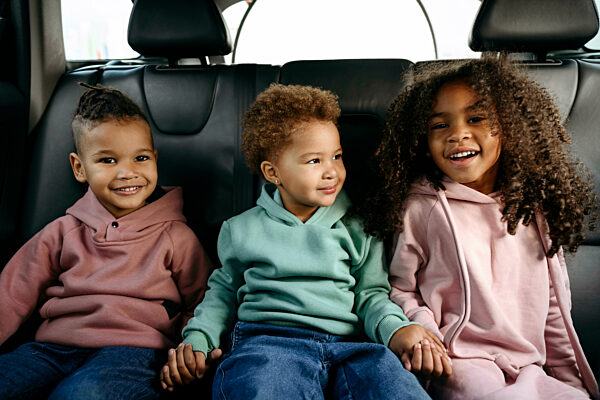 Smiling siblings holding hands on back seat in car