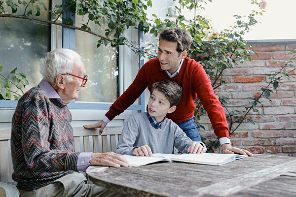 Smiling man and boy looking at senior father talking in backyard