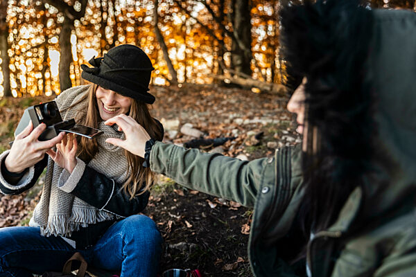 Happy young women taking photographs in autumn forest