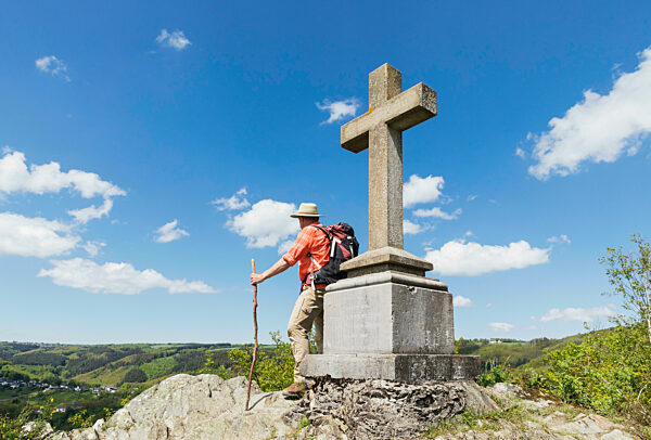Active senior man with hiking stick standing near Summit Cross, Simmerath, Eifel, North Rhine Westphalia, Germany