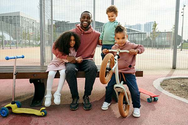 Happy father sitting with arm around children at sports field