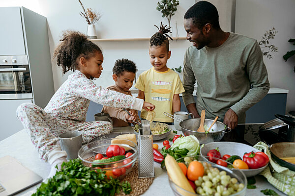 Smiling man looking at sons and daughter making spaghetti in kitchen