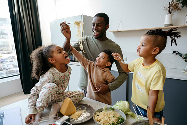 Happy man feeding spaghetti to daughter in kitchen