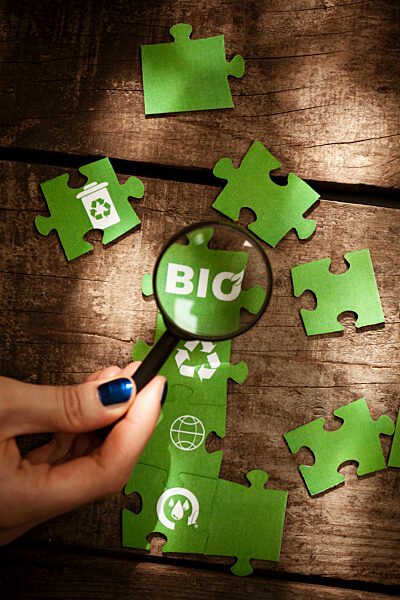 Woman holding magnifying glass over Bio text on green puzzle piece