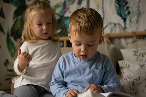 Cute boy with book and twin sister in bedroom at home