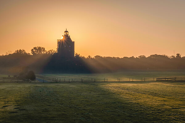 Germany, Hamburg, Sun setting over empty pasture in front of Great Tower Neuwerk lighthouse