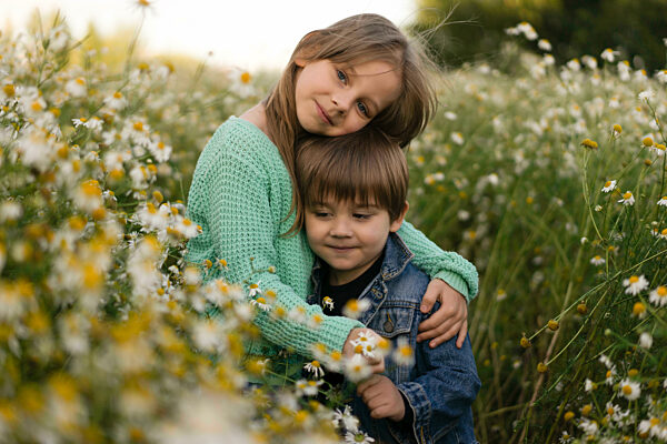 Girl with arm around brother standing amidst flowers in meadow