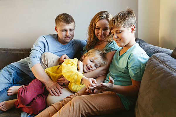 Smiling boy touching finger of brother with parents on sofa