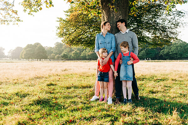 Smiling parents with daughter standing in front of tree on sunny day
