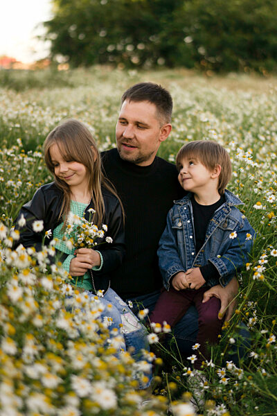 Father with son and daughter crouching by flowers in meadow