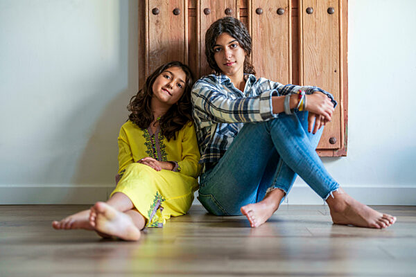 Sisters sitting in front of door at home