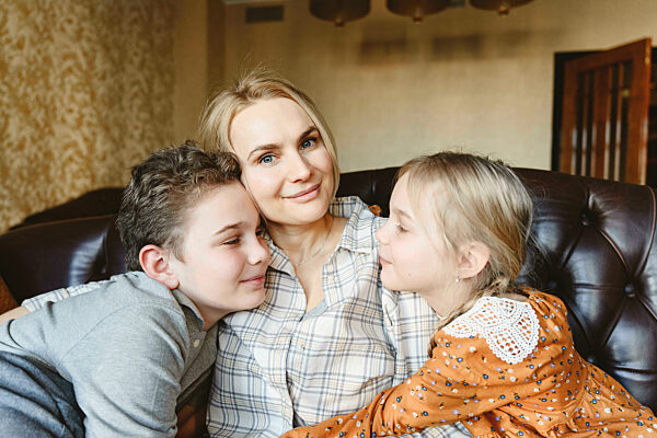 Smiling mother with daughter and son sitting on sofa at home