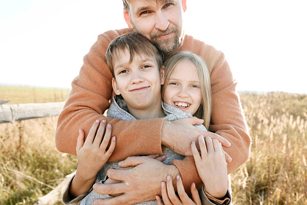 Father embracing smiling daughter and son on sunny day