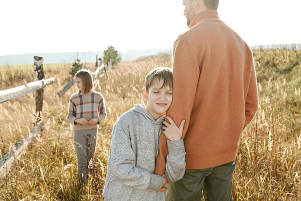 Smiling boy with eyes closed holding hand of father with sister in background