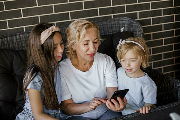 Grandmother sharing smart phone with granddaughters on sofa