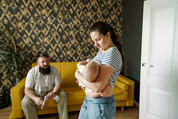 Father looking at mother breastfeeding daughter at home