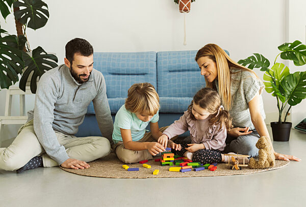 Brother and sister playing toy blocks with parents in living room