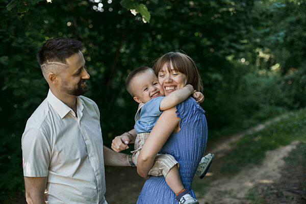 Happy mother embracing son standing by man at park