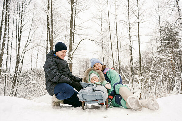 Father and mother with daughter enjoying snow in winter forest