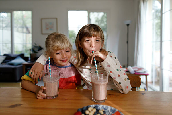 Happy sisters drinking smoothie at home