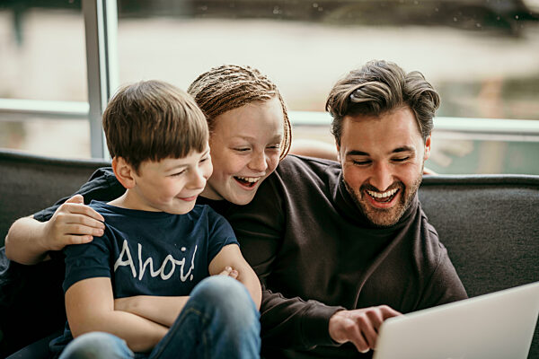 Happy man pointing on laptop sitting with sons at home