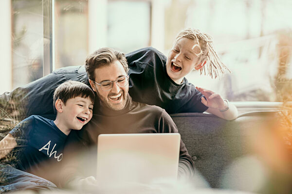 Cheerful man with sons sharing laptop at home