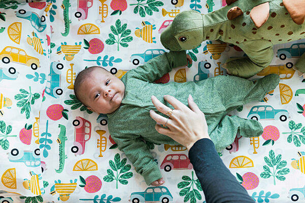 Mother's hand on baby boy lying with toys in bedroom
