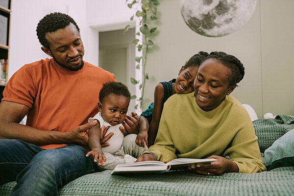 Smiling mother reading book by family in bedroom