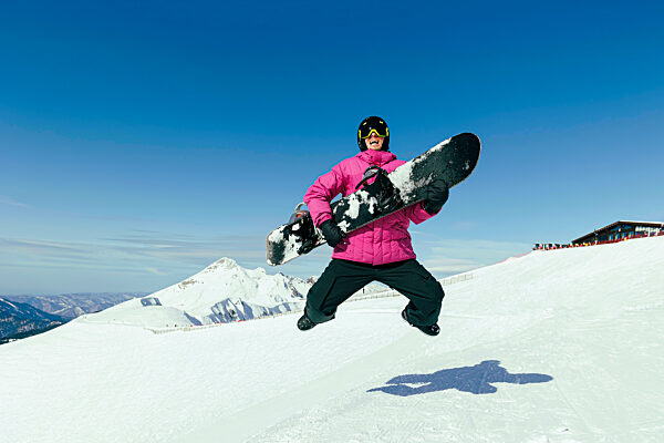Happy man with snowboard jumping on snow in winter