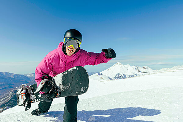 Man with snowboard screaming on snowy mountain on sunny day
