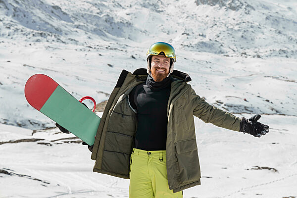 Happy young man with arms outstretched standing on snowcapped mountain