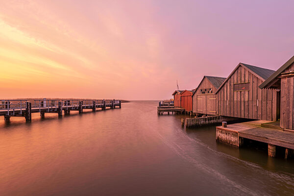 Germany, Mecklenburg-Western Pomerania, Zingst, Pier and row of coastal boathouses at moody dusk