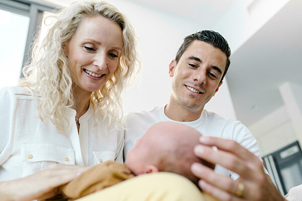 Smiling mother carrying baby on lap sitting by man at home