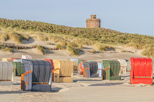 Germany, Lower Saxony, Juist, Hooded beach chairs on empty beach with water tower in background