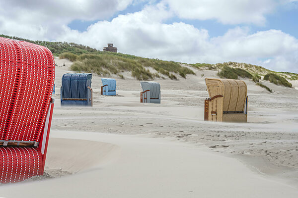 Germany, Lower Saxony, Juist, Hooded beach chairs on empty beach with dunes in background