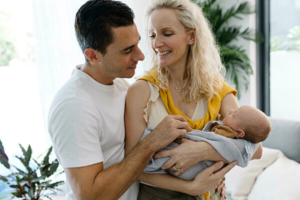 Smiling woman carrying baby in arm sitting by man at home