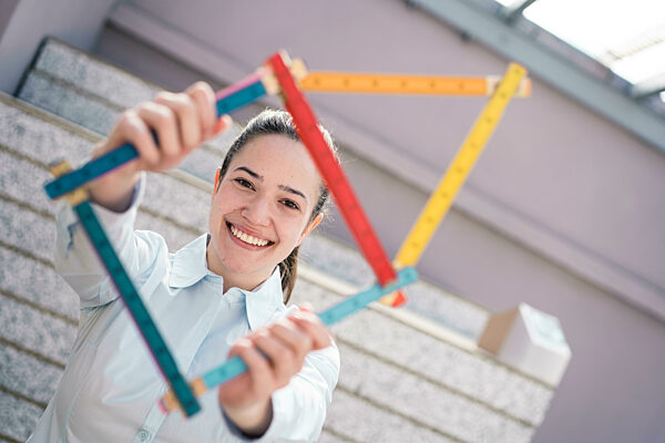 Young female architect making house shape with folding ruler at factory