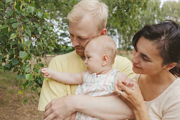 Baby girl touching plant leaves with parents in park